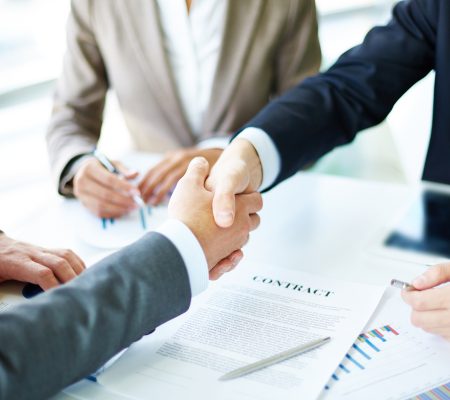 Image of business partners handshaking over business objects on workplace